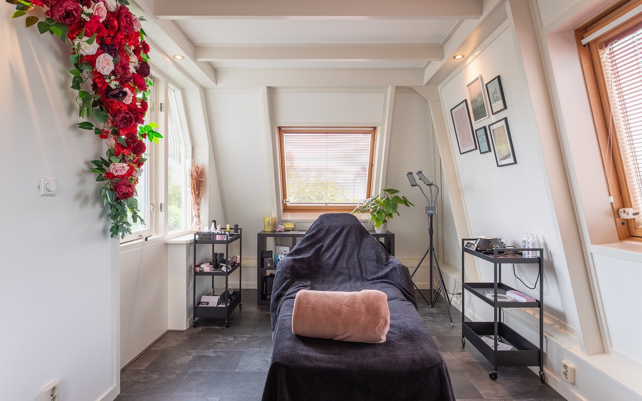 De behandelruimte van Shai Beauty: de behandelbank met roze kussen, de rozenboog en het raam