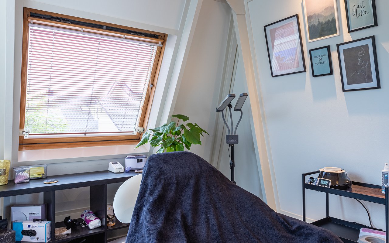 Behandelbank onder het dakraam met ingelijste prints en de wimperlamp